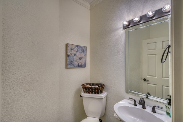 half bathroom with a textured wall, ornamental molding, a sink, and toilet