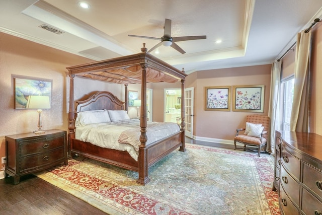 bedroom with ornamental molding, a tray ceiling, wood finished floors, and visible vents