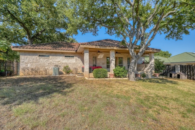 view of front of property featuring stone siding, ceiling fan, fence, a front lawn, and central AC