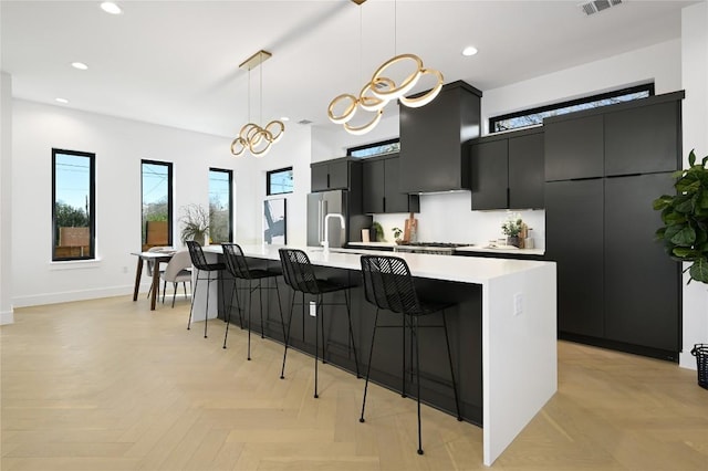 kitchen with a large island, a breakfast bar, light countertops, dark cabinetry, and premium range hood