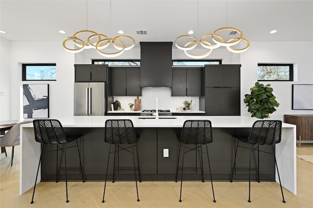 kitchen with high end refrigerator, visible vents, light countertops, a large island with sink, and pendant lighting