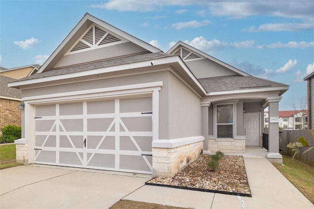 view of front facade with a shingled roof, concrete driveway, stone siding, an attached garage, and stucco siding