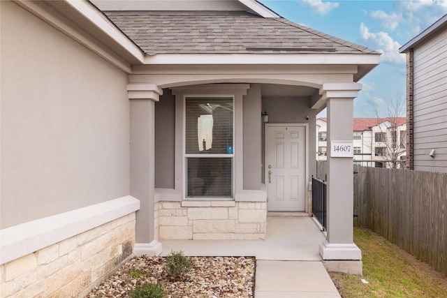 property entrance featuring stone siding, a shingled roof, fence, and stucco siding