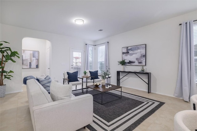 living room with light tile patterned floors, visible vents, arched walkways, and baseboards