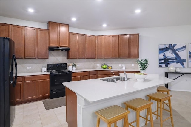 kitchen featuring a breakfast bar area, under cabinet range hood, a sink, decorative backsplash, and black appliances