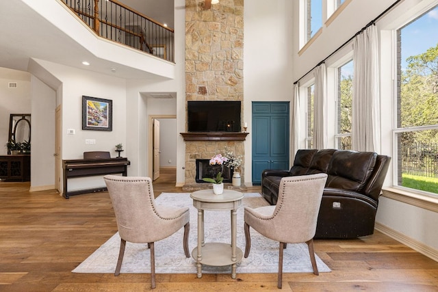 living room with a wealth of natural light, a stone fireplace, baseboards, and wood finished floors