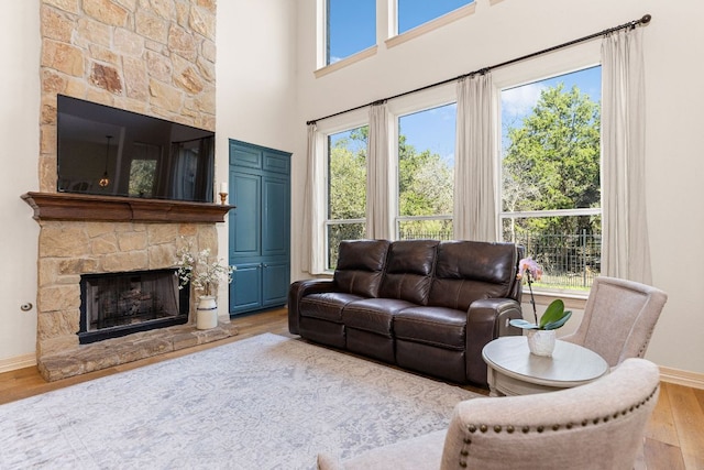 living room featuring a high ceiling, a fireplace, baseboards, and wood finished floors