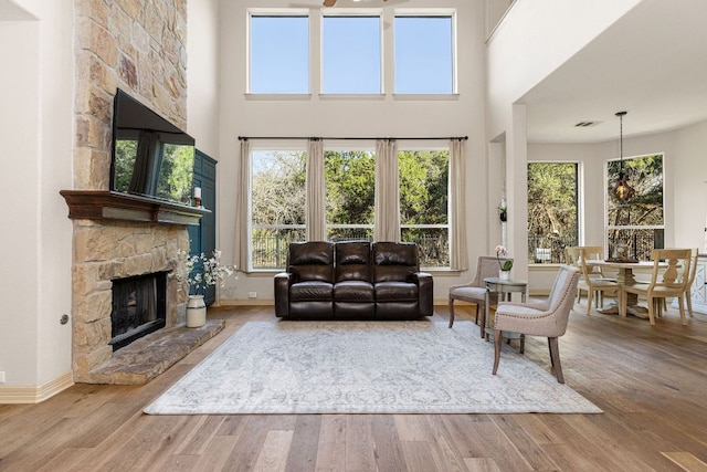 living area featuring a stone fireplace, wood finished floors, visible vents, a towering ceiling, and baseboards