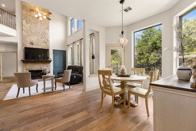 dining room with baseboards, visible vents, hardwood / wood-style flooring, a high ceiling, and a stone fireplace