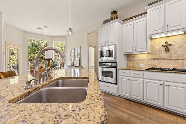 kitchen with visible vents, wood finished floors, a sink, stainless steel appliances, and backsplash