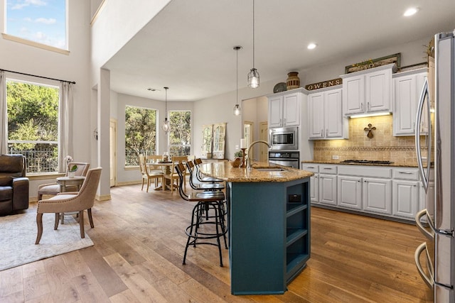 kitchen with stainless steel appliances, a wealth of natural light, tasteful backsplash, white cabinets, and light wood-type flooring