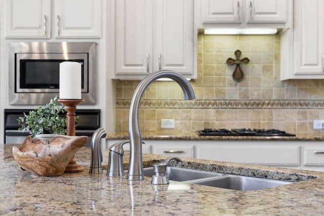 kitchen with white cabinets, stainless steel microwave, decorative backsplash, and light stone countertops