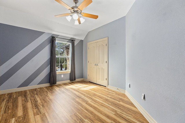 unfurnished bedroom with lofted ceiling, ceiling fan, light wood-style flooring, baseboards, and a closet