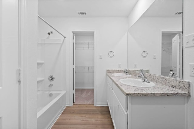 full bath with shower / bath combination, double vanity, a sink, and wood finished floors