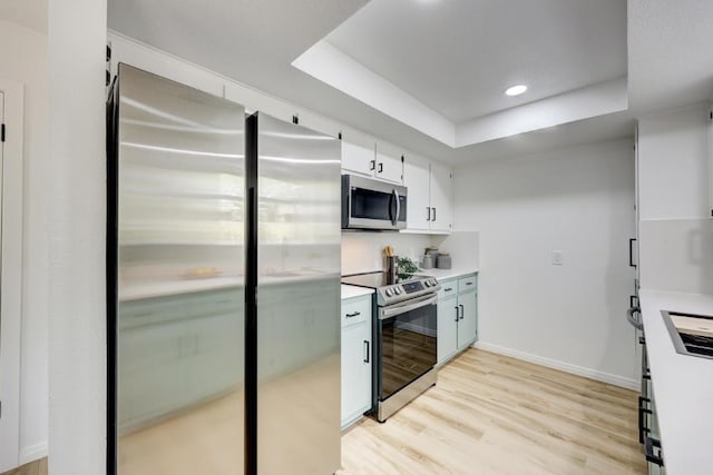 kitchen with a tray ceiling, stainless steel appliances, light countertops, light wood-style floors, and white cabinetry