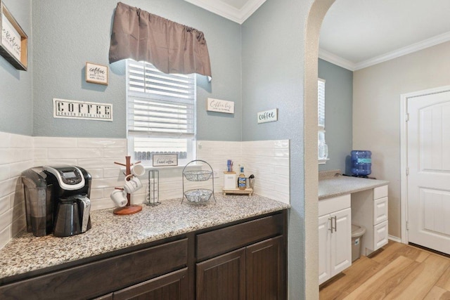 interior space with arched walkways, light stone counters, dark brown cabinets, ornamental molding, and light wood finished floors