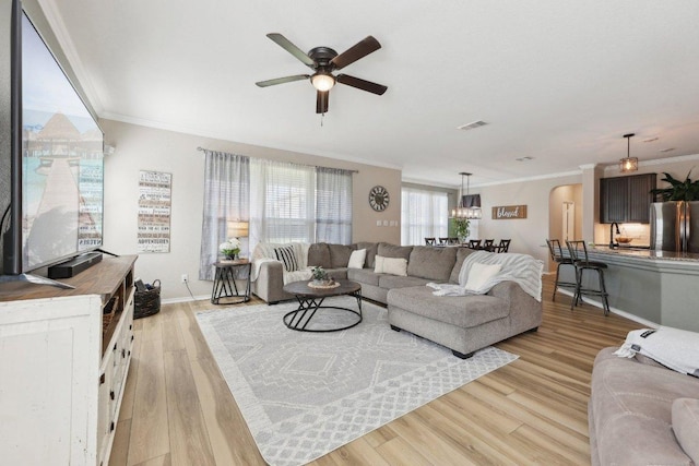 living room with arched walkways, crown molding, visible vents, light wood-type flooring, and baseboards