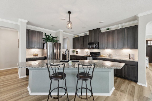 kitchen featuring arched walkways, light wood-type flooring, black appliances, a kitchen bar, and a sink