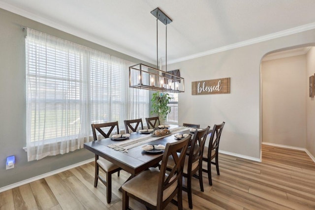 dining area featuring light wood finished floors, baseboards, arched walkways, ornamental molding, and a chandelier