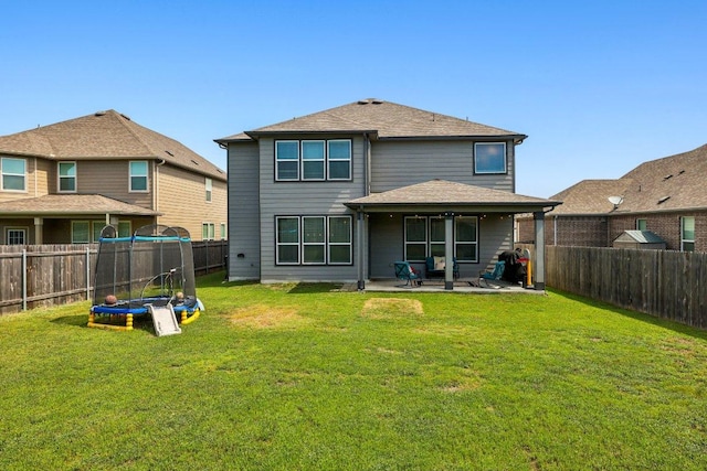 back of house with a trampoline, a patio area, a fenced backyard, and a lawn