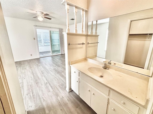 bathroom with a textured ceiling, wood finished floors, visible vents, vanity, and a ceiling fan