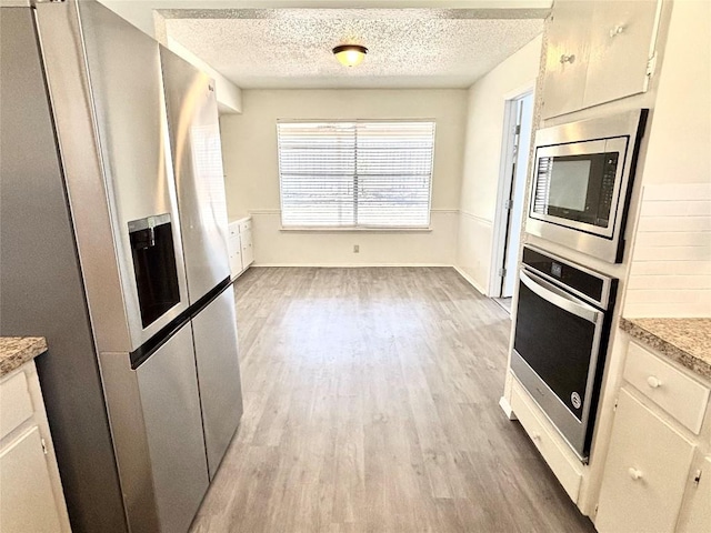 kitchen with stainless steel appliances, light countertops, light wood-style floors, white cabinetry, and a textured ceiling