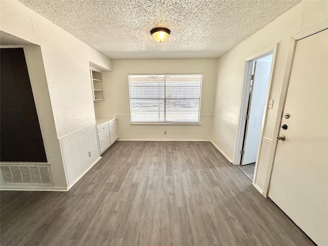 interior space with a wainscoted wall, a textured ceiling, visible vents, and dark wood-style flooring