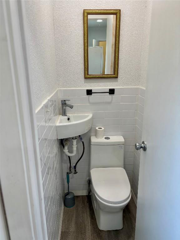 half bath featuring toilet, a wainscoted wall, wood finished floors, a sink, and tile walls