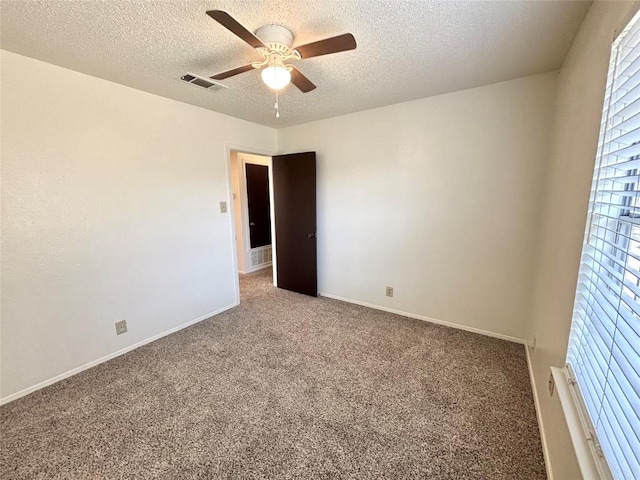 carpeted empty room with a textured ceiling, a ceiling fan, visible vents, and baseboards