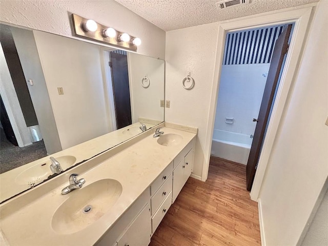 bathroom featuring a textured ceiling, a sink, and wood finished floors