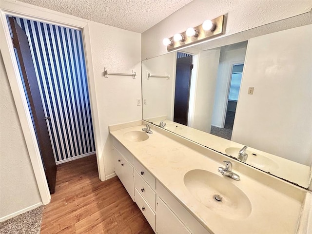 full bathroom featuring double vanity, a textured ceiling, a sink, and wood finished floors