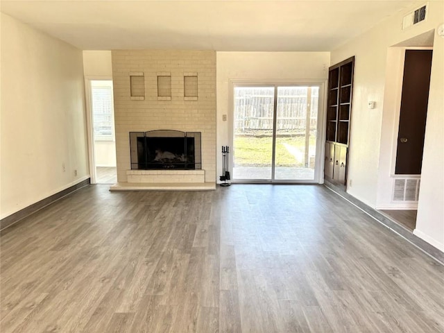 unfurnished living room featuring a brick fireplace, wood finished floors, visible vents, and baseboards