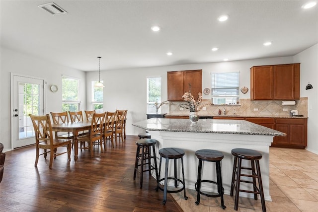 kitchen with visible vents, decorative backsplash, a breakfast bar area, brown cabinets, and a center island