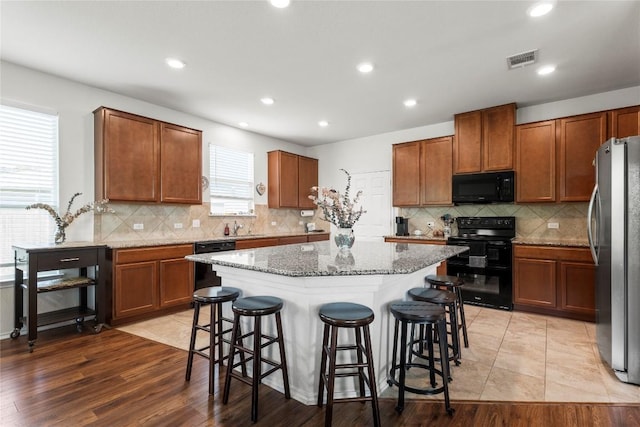 kitchen with a breakfast bar, a center island, black appliances, and light stone countertops