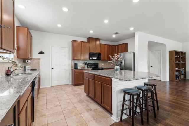 kitchen with black appliances, a breakfast bar area, light stone counters, and a center island