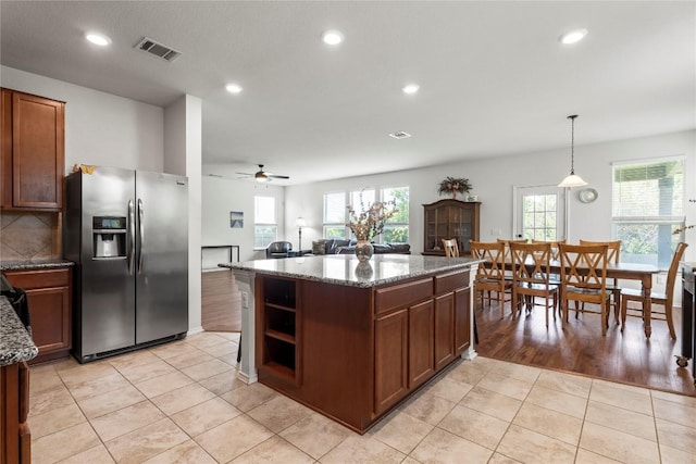 kitchen featuring light tile patterned floors, visible vents, decorative backsplash, stainless steel fridge with ice dispenser, and a kitchen island