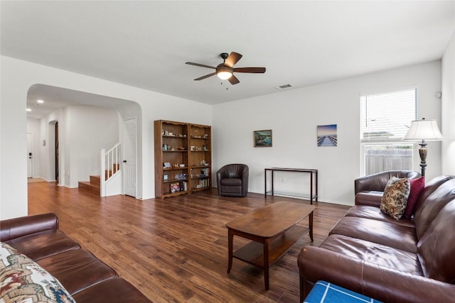 living area with ceiling fan, arched walkways, wood finished floors, visible vents, and stairs