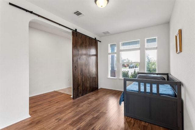 bedroom with a barn door, wood finished floors, visible vents, and baseboards