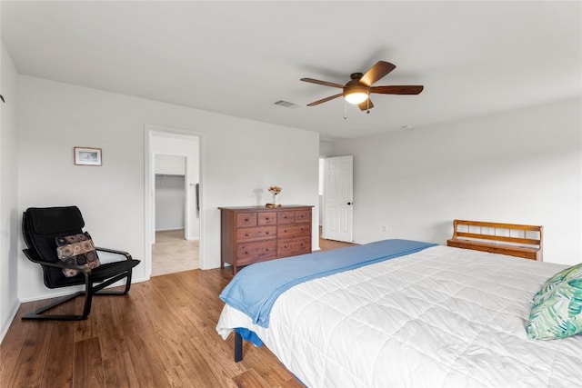 bedroom with a walk in closet, a closet, visible vents, ceiling fan, and wood finished floors