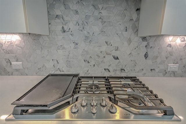 interior details with white cabinets, wall chimney exhaust hood, stainless steel gas stovetop, and decorative backsplash