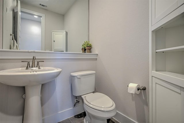 half bathroom with visible vents, toilet, a sink, baseboards, and tile patterned floors