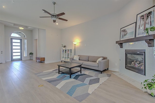 living area with light wood-style floors, a fireplace with flush hearth, baseboards, and ceiling fan