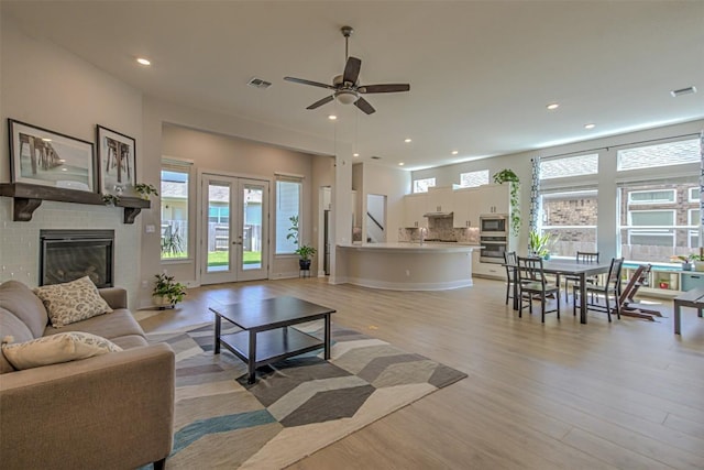 living area featuring light wood-type flooring, recessed lighting, french doors, and a glass covered fireplace