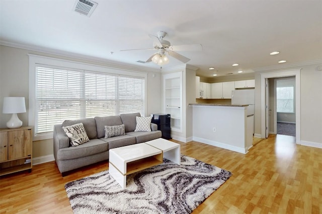 living room with ornamental molding, visible vents, light wood-style flooring, and baseboards