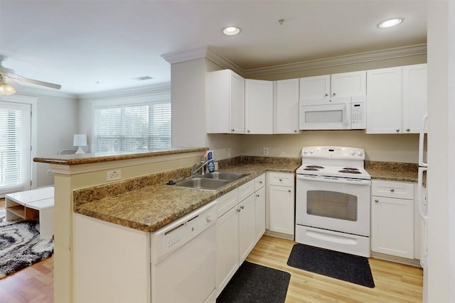 kitchen featuring a peninsula, white appliances, a sink, light wood finished floors, and crown molding