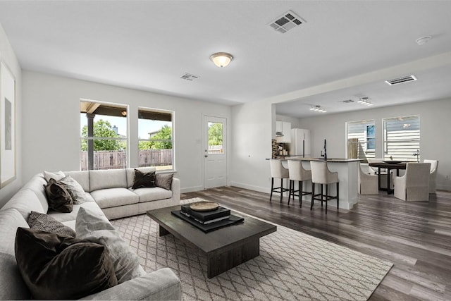 living room with dark wood-style flooring, visible vents, and baseboards