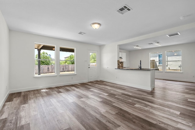 unfurnished living room featuring baseboards, visible vents, and wood finished floors