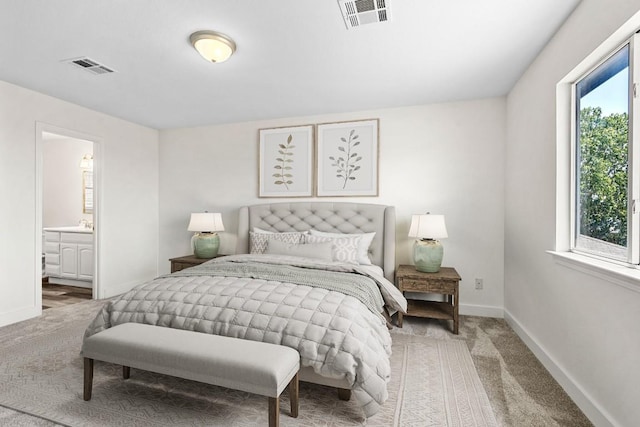 bedroom with light colored carpet, visible vents, ensuite bath, and baseboards