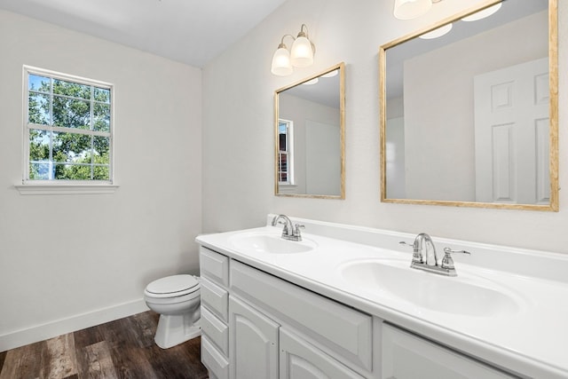 bathroom featuring double vanity, toilet, a sink, and wood finished floors