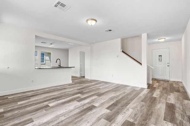 unfurnished living room featuring stairway, a sink, visible vents, and light wood-style floors